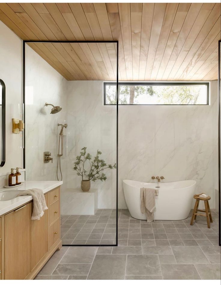 a bathroom with a tub, sink and mirror in it's center wall that has wood paneling on the ceiling