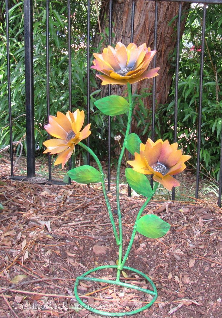 three flowers are growing in the ground near a fence