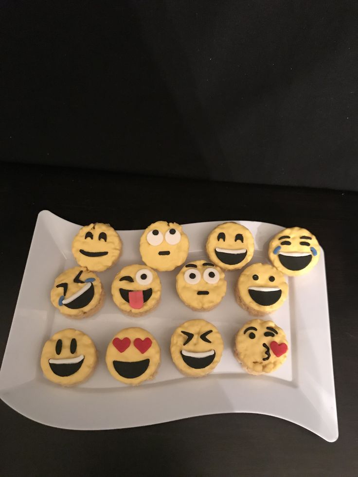 a white plate topped with lots of cookies covered in emoticions on top of a table