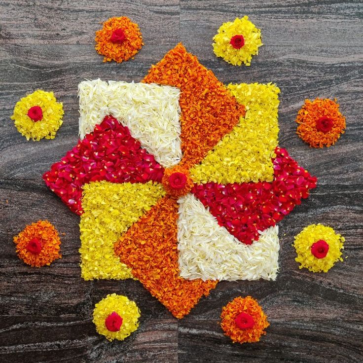 an arrangement of flowers and petals arranged on a wooden surface with red, yellow, orange, and white colors