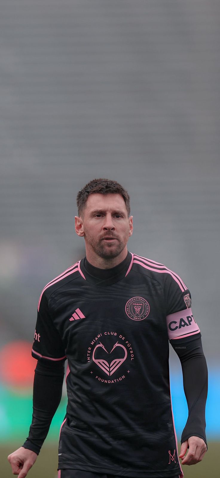 a man standing on top of a soccer field wearing a black uniform and holding a soccer ball