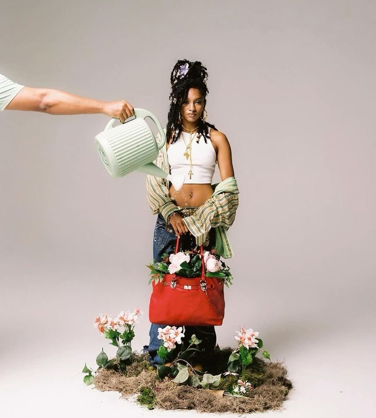 a woman holding a watering can next to a red purse