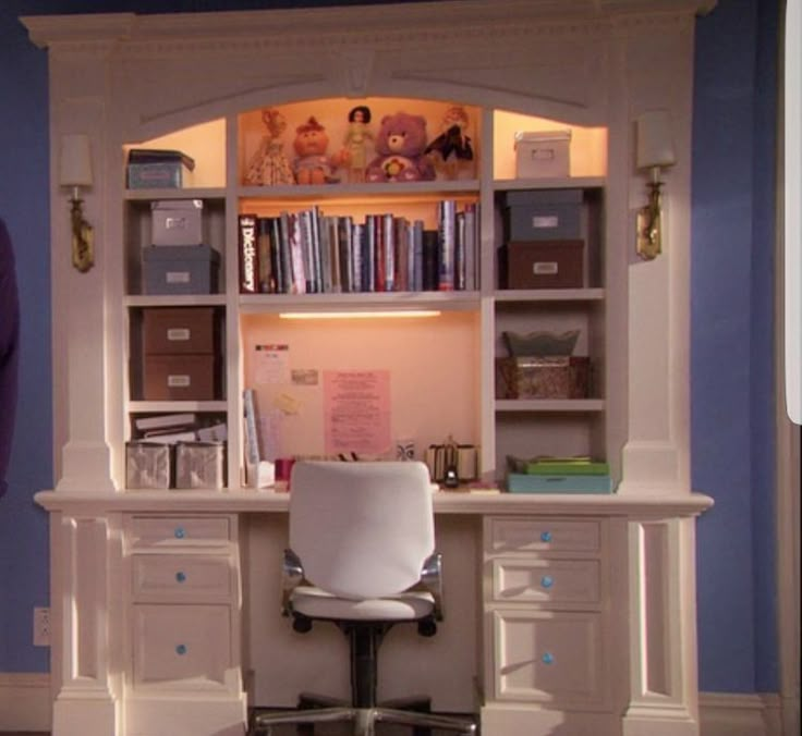 a white desk and chair in front of a book shelf with books on top of it