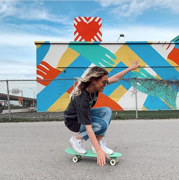 a woman riding a skateboard down the middle of a street next to a fence