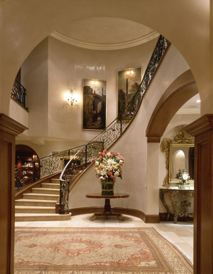 an elegant foyer with stairs and paintings on the walls, along with a vase filled with flowers