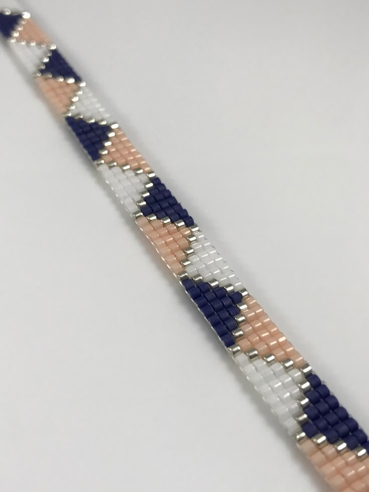 a close up of a bracelet on a white surface with blue, pink and silver beads