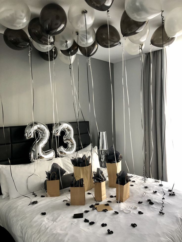 some balloons are hanging from the ceiling above a bed with black and white decorations on it