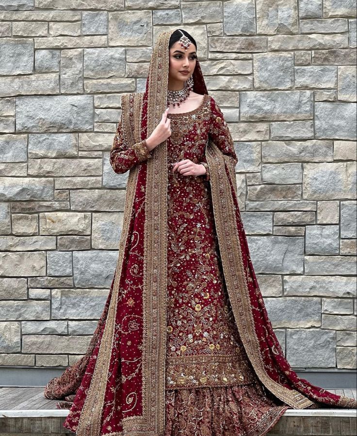 a woman standing in front of a brick wall wearing a red and gold bridal gown