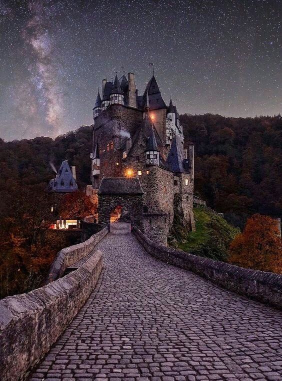 the night sky is shining brightly over an old castle on a cobblestone road