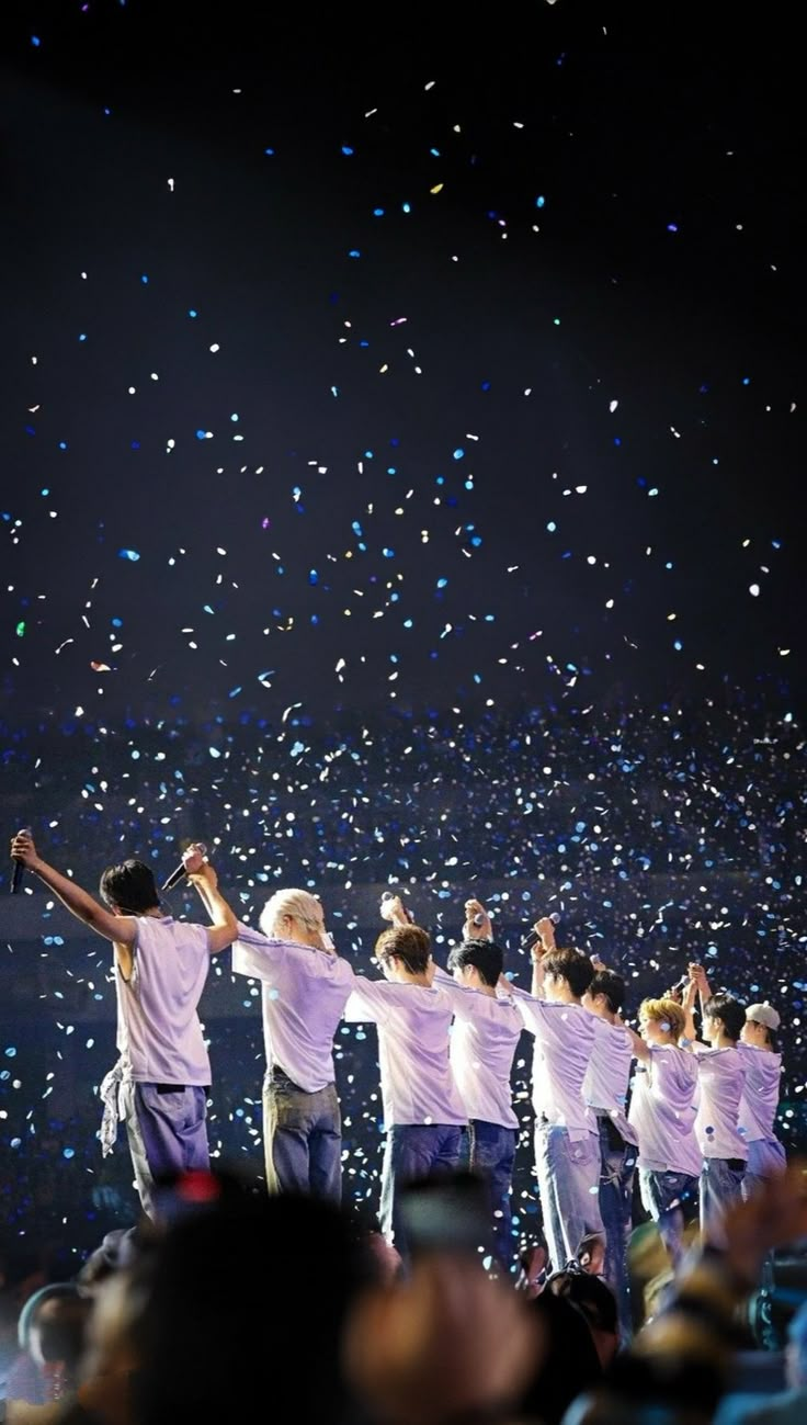 a group of men standing on top of a stage holding hands up in the air