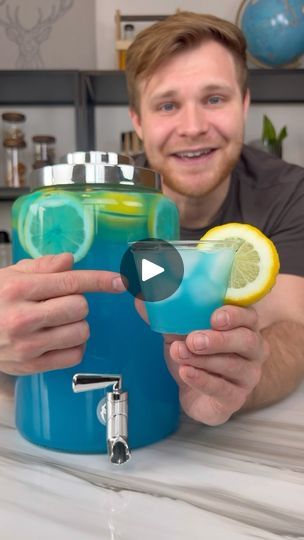 a man is holding up two glasses with lemons and blue liquid in front of him