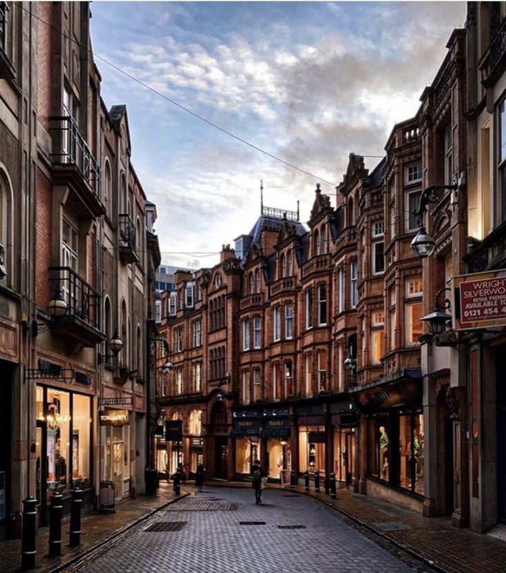 a cobblestone street in an old european city at dusk with people walking on the sidewalk