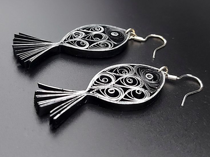 two black fish shaped earrings are shown on a dark surface with silver earwires