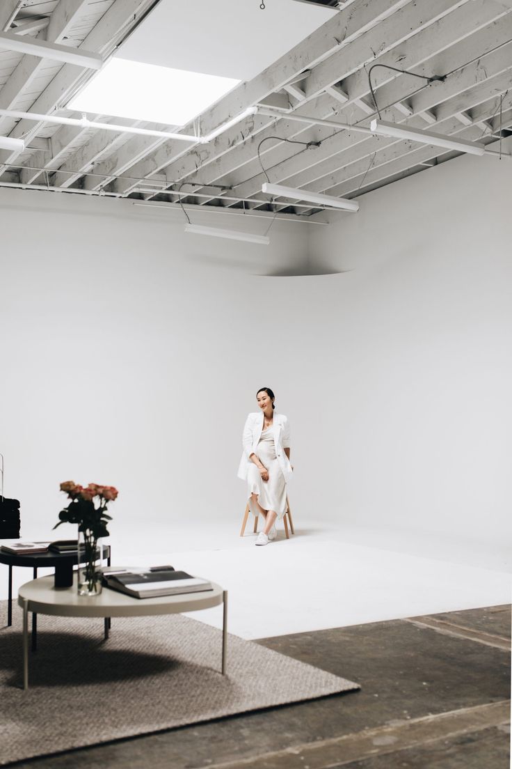 a woman sitting on a chair in front of a white backdrop with flowers and a coffee table