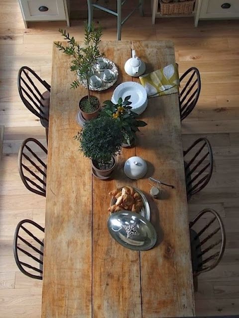 an overhead view of a wooden table with chairs and dishes on it, in the middle of a wood floored dining room