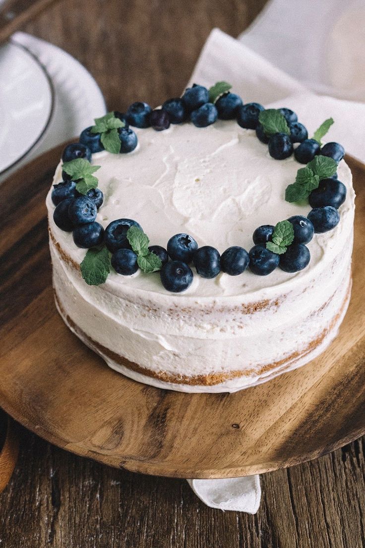 a cake with white frosting and blueberries on a wooden platter next to silverware