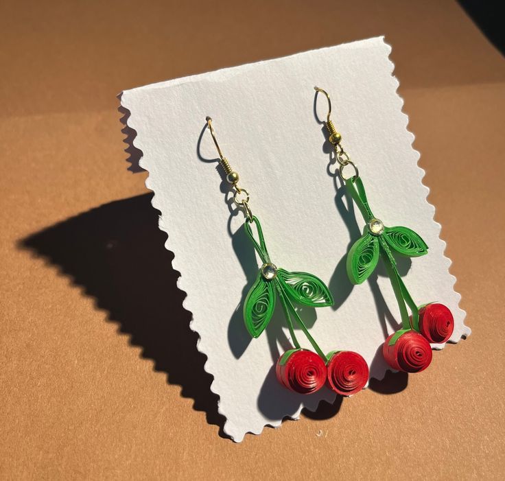 the earrings are made out of paper and have red flowers on them with green leaves