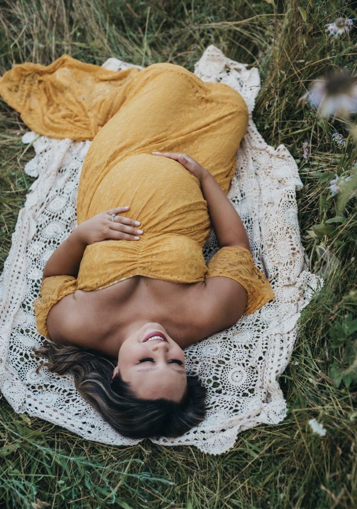 a pregnant woman laying on top of a white doily in the middle of grass