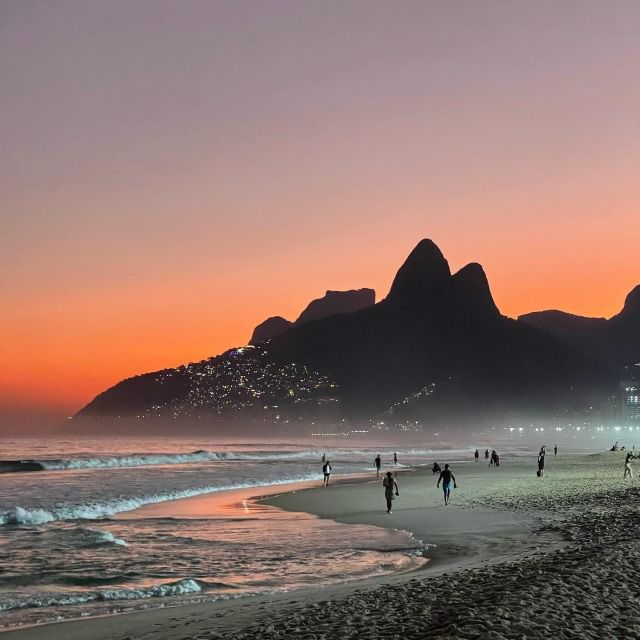 people walking on the beach at sunset with mountains in the backgrounnds