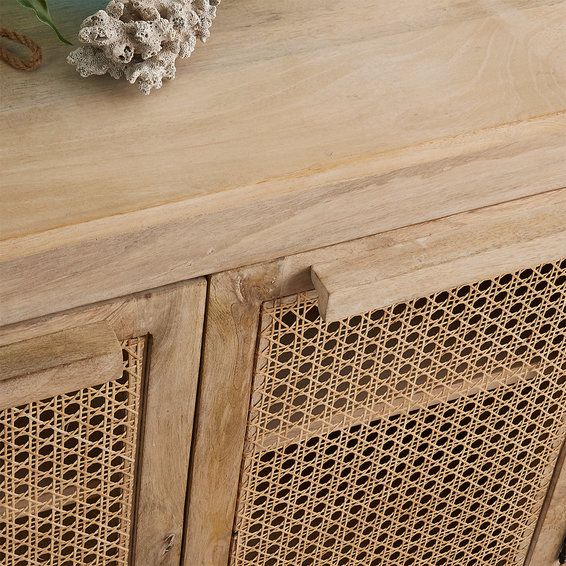 a vase with flowers sitting on top of a wooden table next to a wicker cabinet