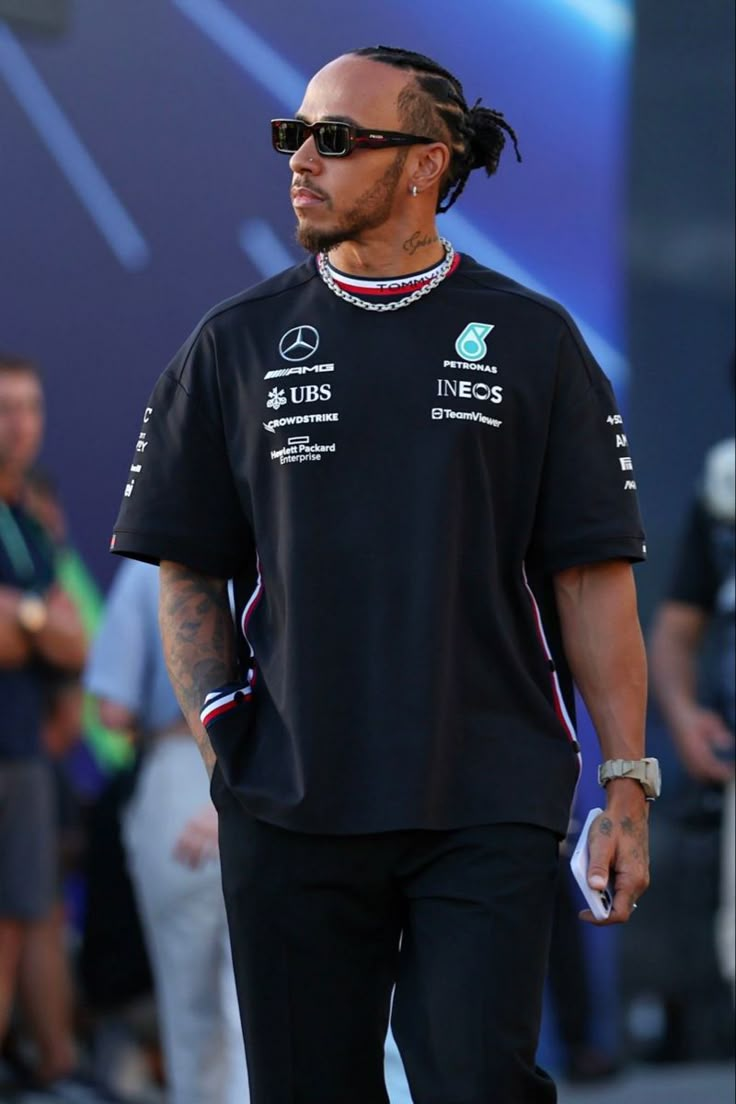 a man with dreadlocks walking down the street wearing a black shirt and sunglasses