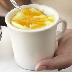 a person holding a white cup filled with orange juice and topped with a spoon in it