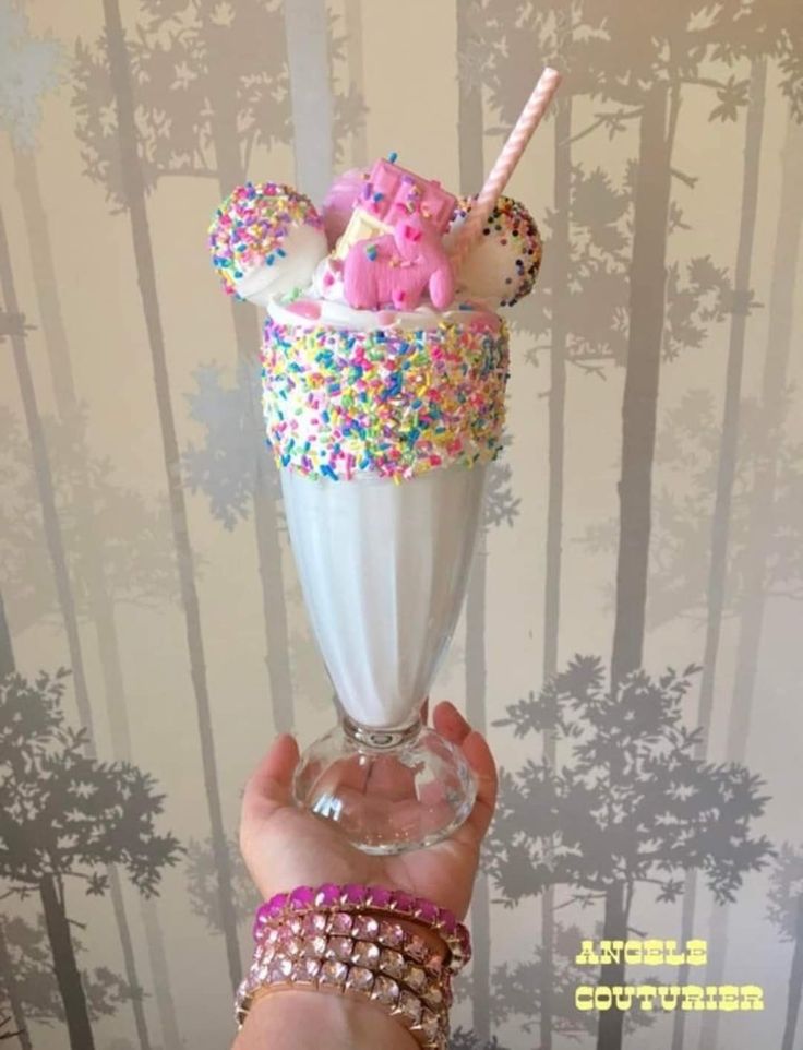 a person holding up a milkshake with sprinkles and pink pigs