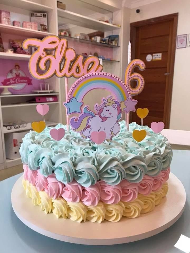 a birthday cake decorated with pastel icing and a rainbow unicorn on the top