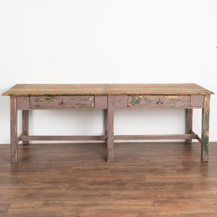 an old wooden table sitting on top of a hard wood floor next to a white wall