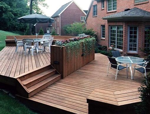 a wooden deck in front of a brick house with an umbrella over the table and chairs