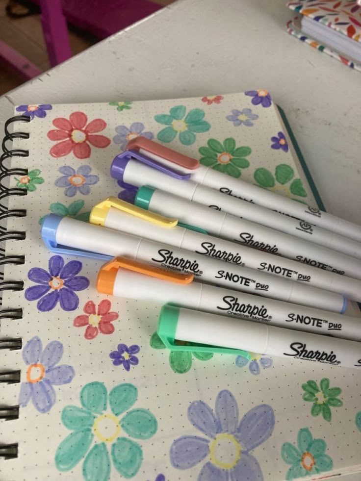 four pens sitting on top of a notebook next to each other in front of flowers