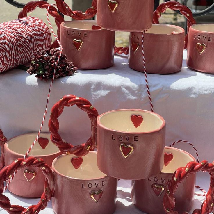 pink ceramic mugs with love written on them are sitting on a white tablecloth