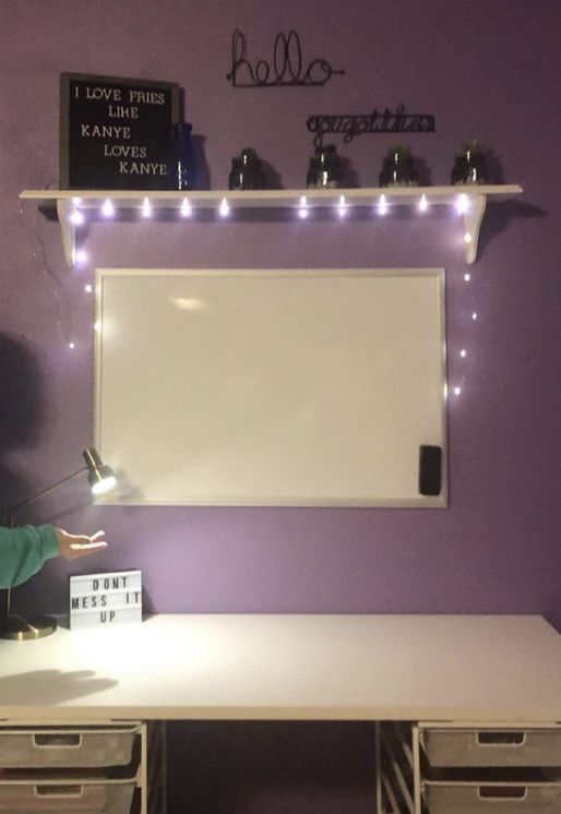 a desk with two drawers and a white board on the wall above it that is lit up by lights