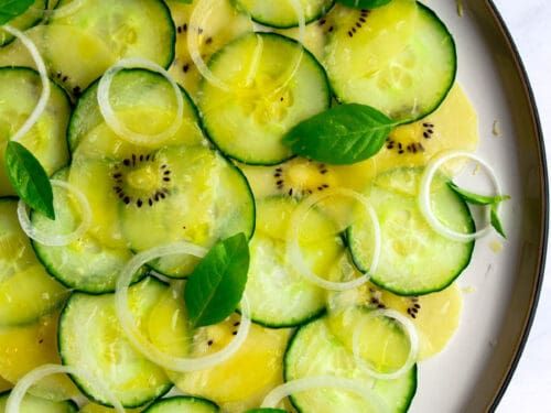 sliced cucumbers and onions are arranged in a dish with green leaves on top