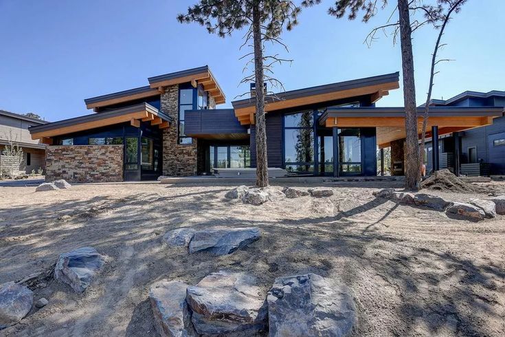 a large house sitting on top of a dirt field next to trees and rocks in front of it