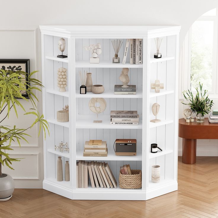 a white book shelf filled with books on top of a hard wood floor next to a potted plant