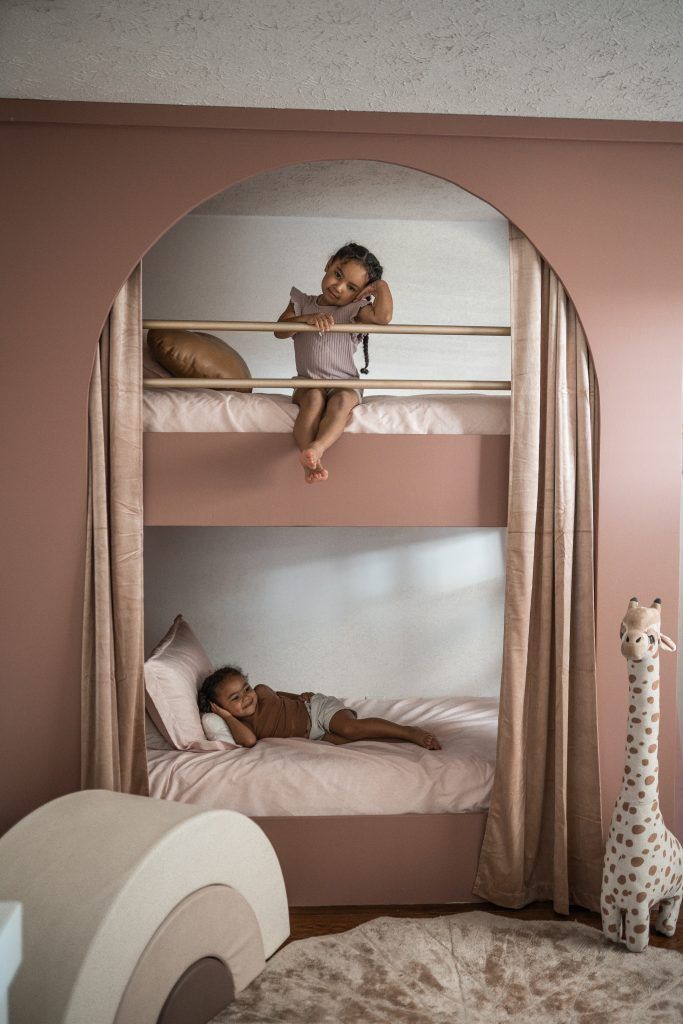 two children sitting on bunk beds in a pink room with giraffes nearby