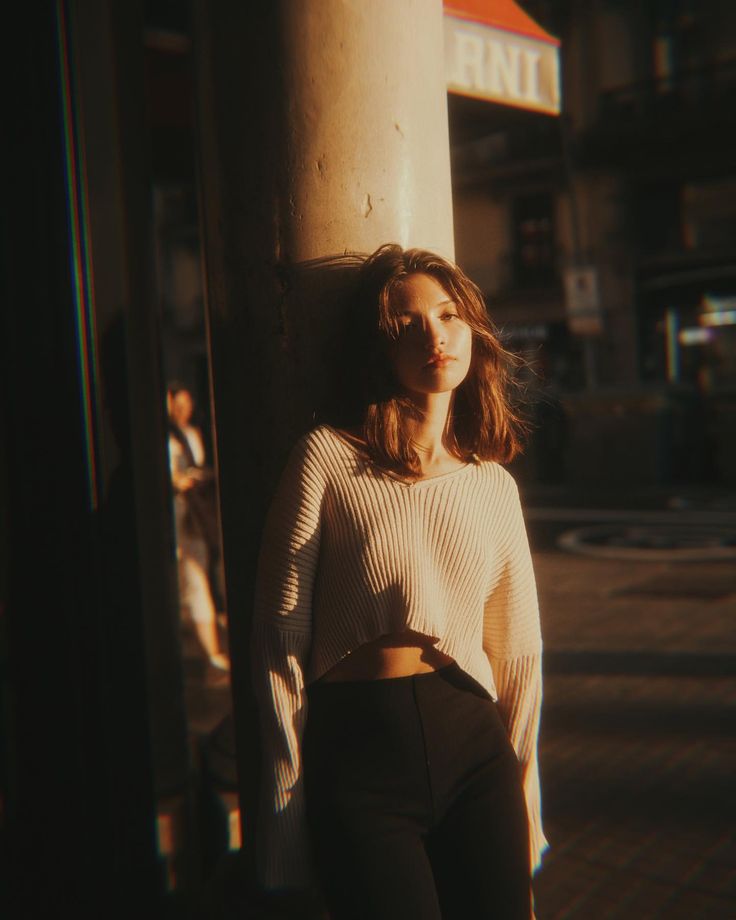 a woman leaning against a pole on the street