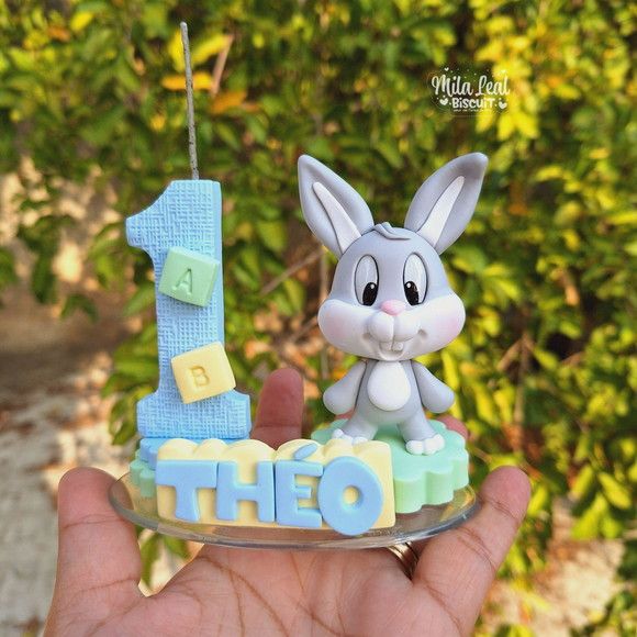 a hand holding up a cake shaped like a bunny and the number one on it