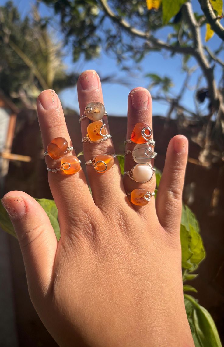 a person's hand with three rings on it and two oranges in the background