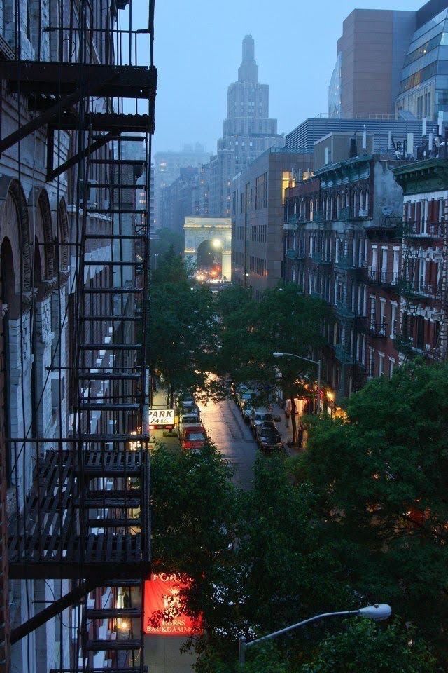 a city street filled with lots of traffic next to tall buildings and trees in the distance