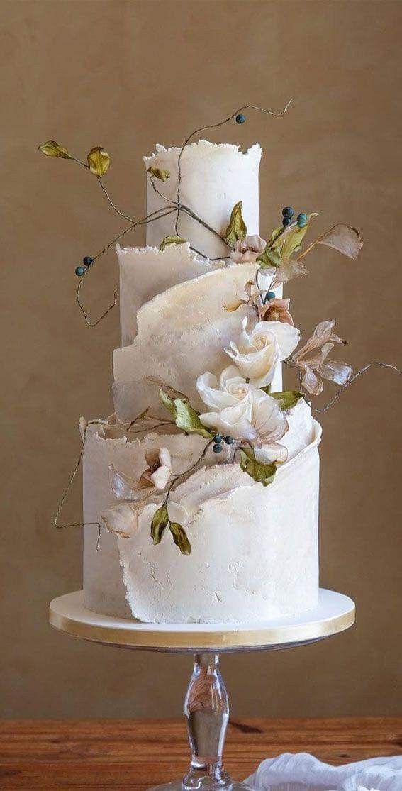 a three tiered wedding cake with flowers on top is sitting on a wooden table