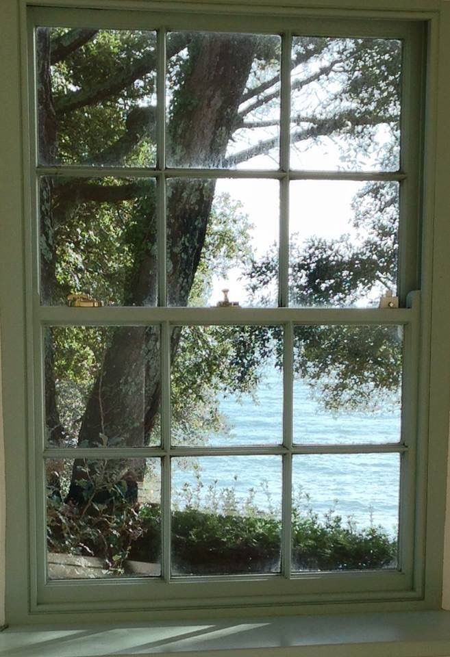 an open window with the view of water and trees from it's windowsill