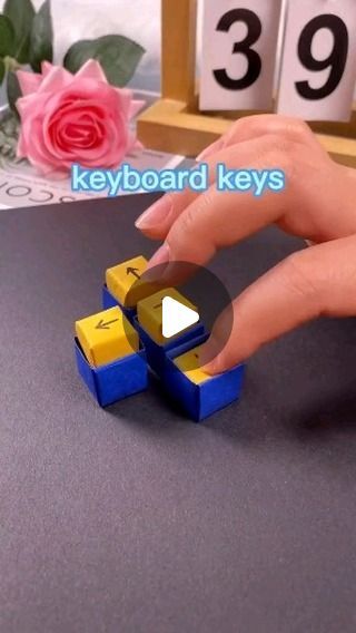 a hand is holding a small yellow and blue object with the word keyboard keys on it