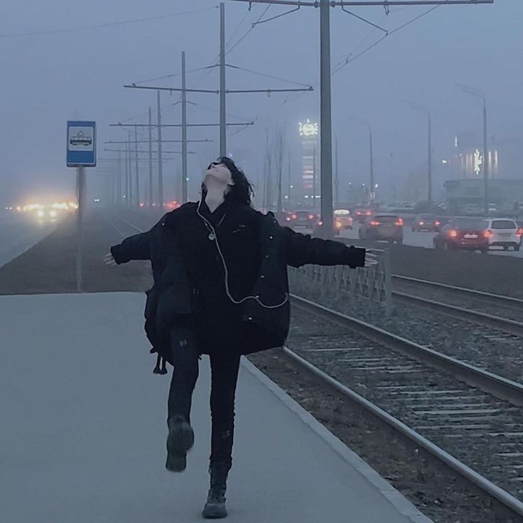 a woman walking down a train track in the rain with her headphones hanging out