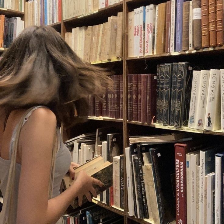 a woman standing in front of a bookshelf with her hair blowing in the wind