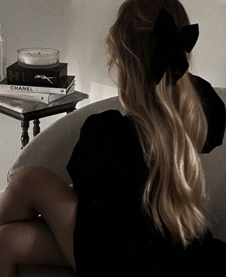 a woman sitting on top of a couch next to a table with books and candles