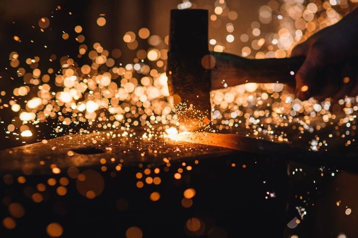 a person using a hammer to cut wood with sparks in the background and blurry lights on the floor