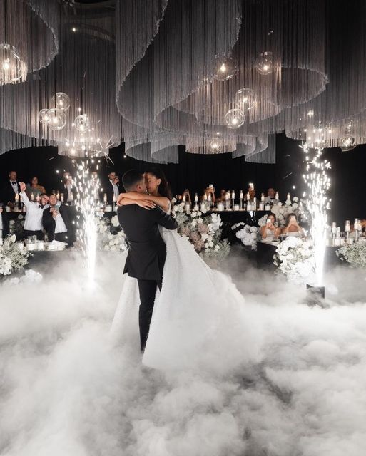 a bride and groom kissing in front of chandeliers with lights hanging from the ceiling