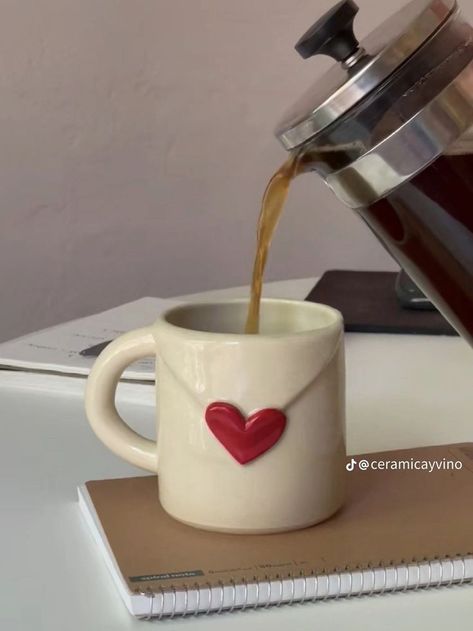 coffee being poured into a mug with a red heart on the front and bottom, next to a notebook